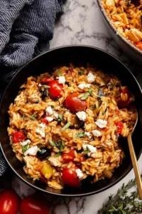 One pot Greek chicken orzo in a cast iron skillet with feta and cherry tomatoes