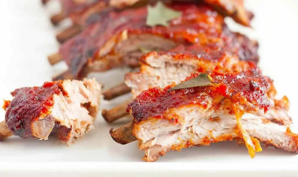 Fall off the bone oven baked ribs glazed with homemade BBQ sauce on a wooden cutting board