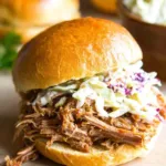 Slow cooker pulled pork piled onto toasted sandwich rolls with creamy coleslaw