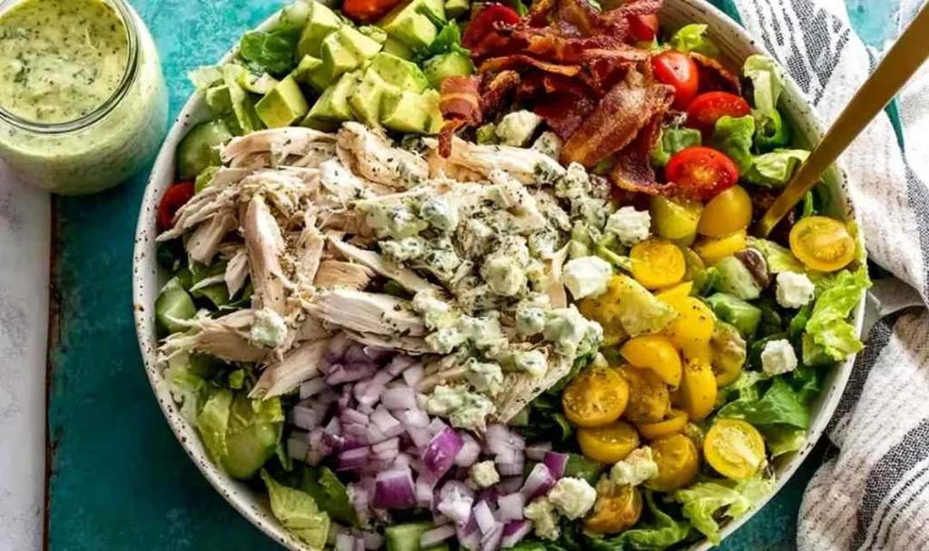 big quick chicken salad in a large bowl with avocado, bacon, and fresh vegetables