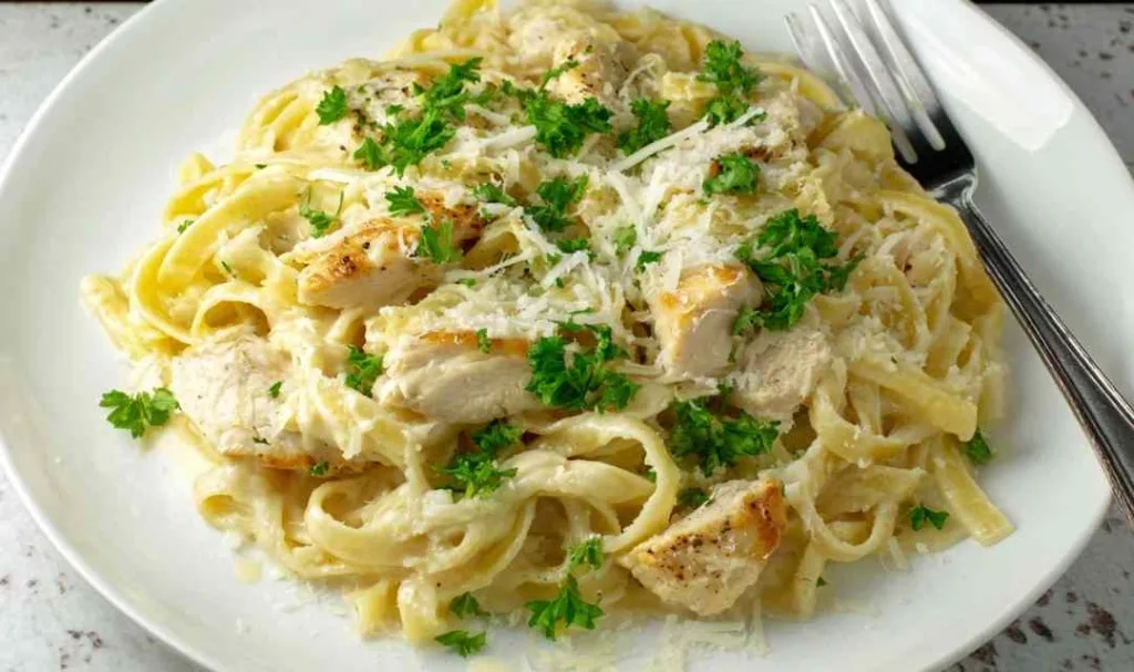 Easy chicken fettuccine alfredo in a white bowl garnished with fresh parsley and cracked black pepper