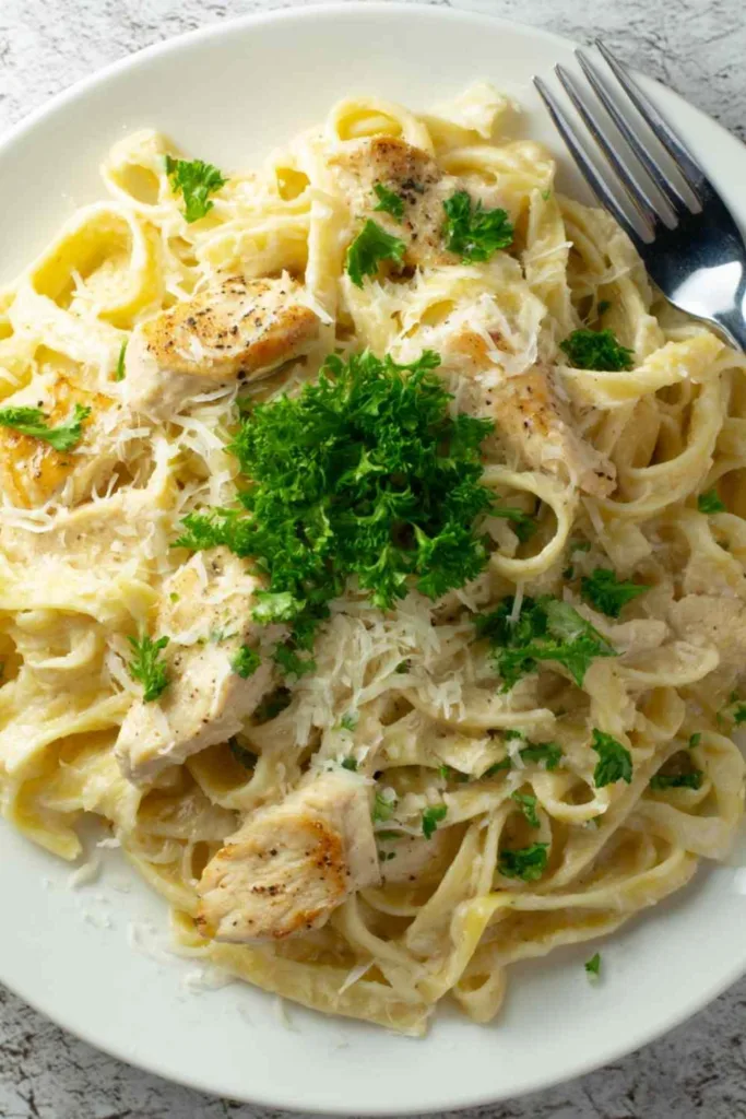 Easy chicken fettuccine alfredo in a white bowl garnished with fresh parsley and cracked black pepper