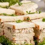 Deli-style chicken sandwiches on a white serving platter garnished with fresh greens