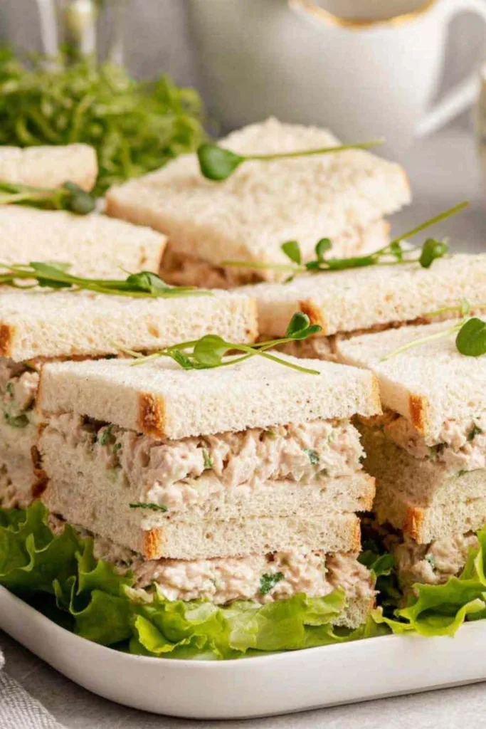 Deli-style chicken sandwiches on a white serving platter garnished with fresh greens