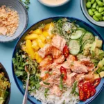 Coconut rice salmon bowl topped with mango, avocado, edamame, cucumber, and coconut lime dressing