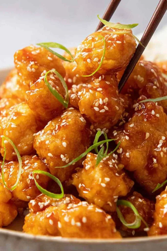 Crispy honey chicken recipe piled on plate with sesame seeds and green onions