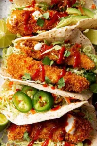 crunchy baked chicken taco fingers on warm flour tortillas with avocado slaw and sriracha