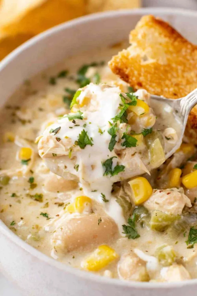 slow cooker creamy white chicken chili in a white bowl topped with cilantro sour cream and lime