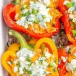 Buffalo chicken stuffed peppers topped with blue cheese and green onions in a glass baking dish