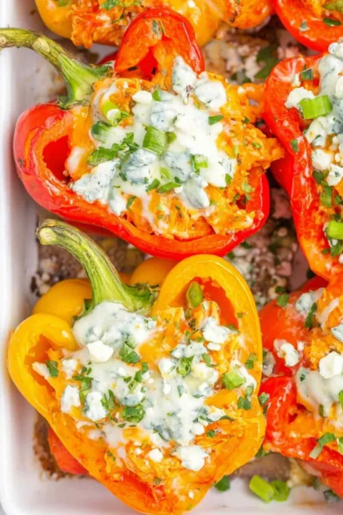 Buffalo chicken stuffed peppers topped with blue cheese and green onions in a glass baking dish