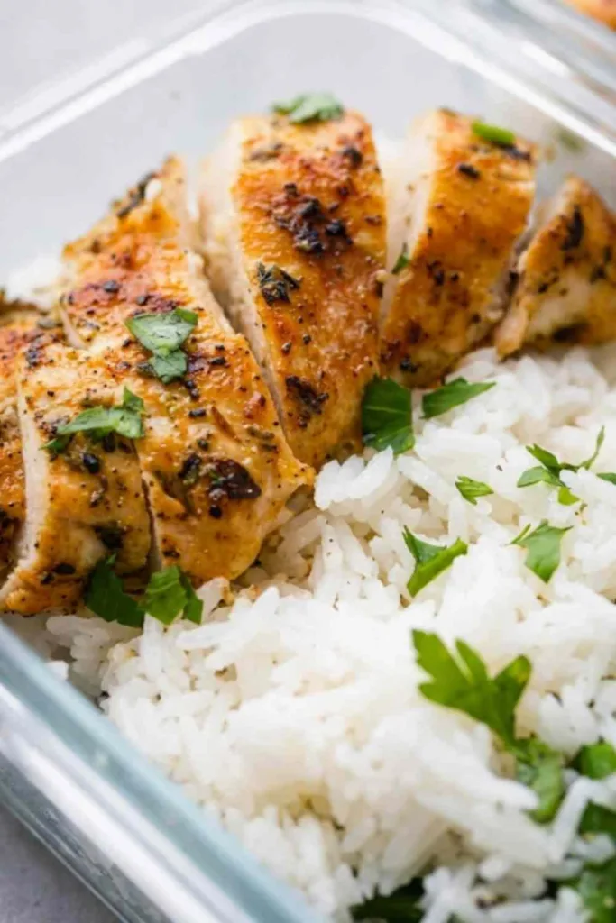 Four airtight meal prep containers filled with sliced chicken and rice meal prep bowls and steamed green beans