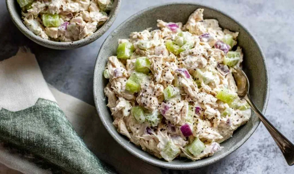 Classic chicken salad recipe served in a white bowl with celery and red onion