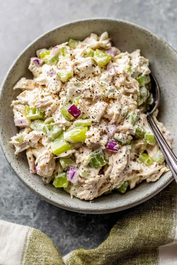 Classic chicken salad recipe served in a white bowl with celery and red onion