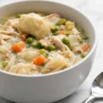A bowl of Crock Pot Chicken and Dumplings with creamy sauce, shredded chicken, and soft biscuit dumplings garnished with fresh parsley