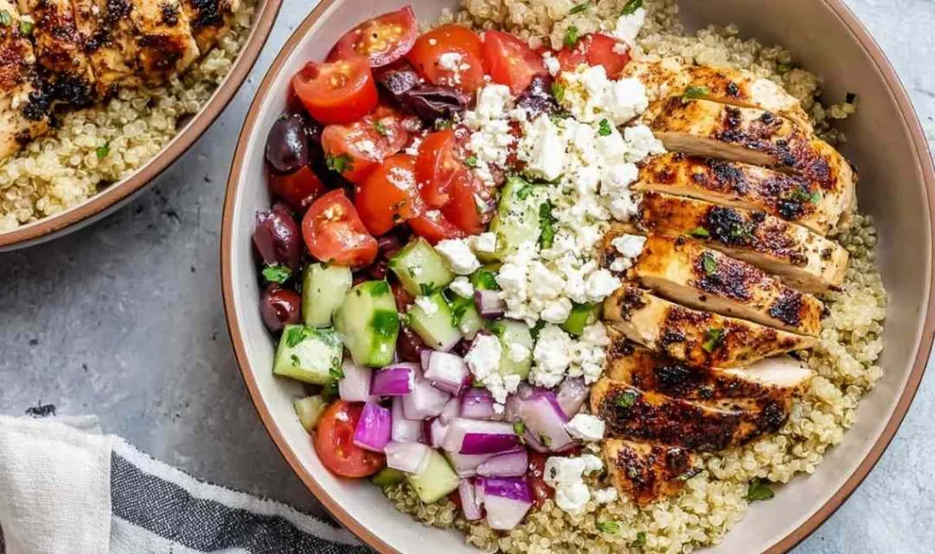 Top view of a Greek chicken bowl with grilled chicken, quinoa, cucumber, tomatoes, feta, and kalamata olives