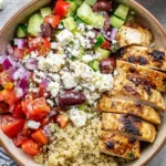 Top view of a Greek chicken bowl with grilled chicken, quinoa, cucumber, tomatoes, feta, and kalamata olives
