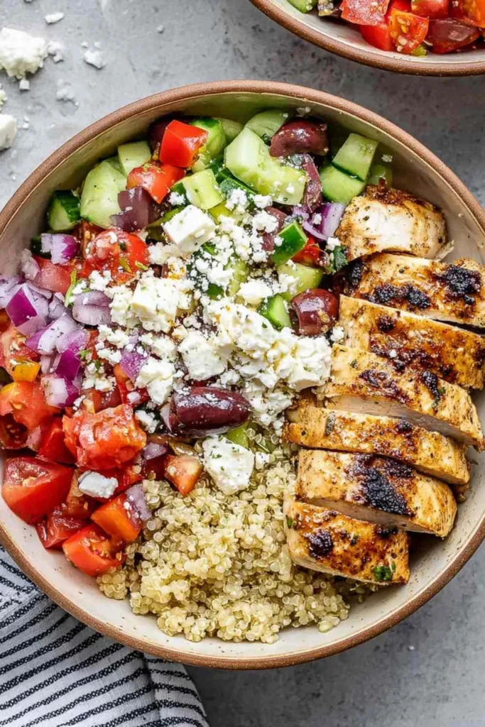 Top view of a Greek chicken bowl with grilled chicken, quinoa, cucumber, tomatoes, feta, and kalamata olives