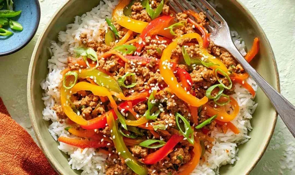 Ground chicken stir fry bowls served over jasmine rice with colorful bell peppers, green onions, and sesame seeds