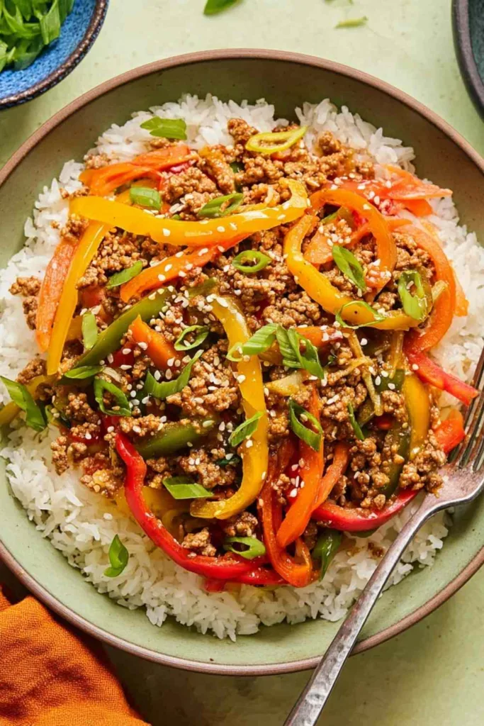Ground chicken stir fry bowls served over jasmine rice with colorful bell peppers, green onions, and sesame seeds