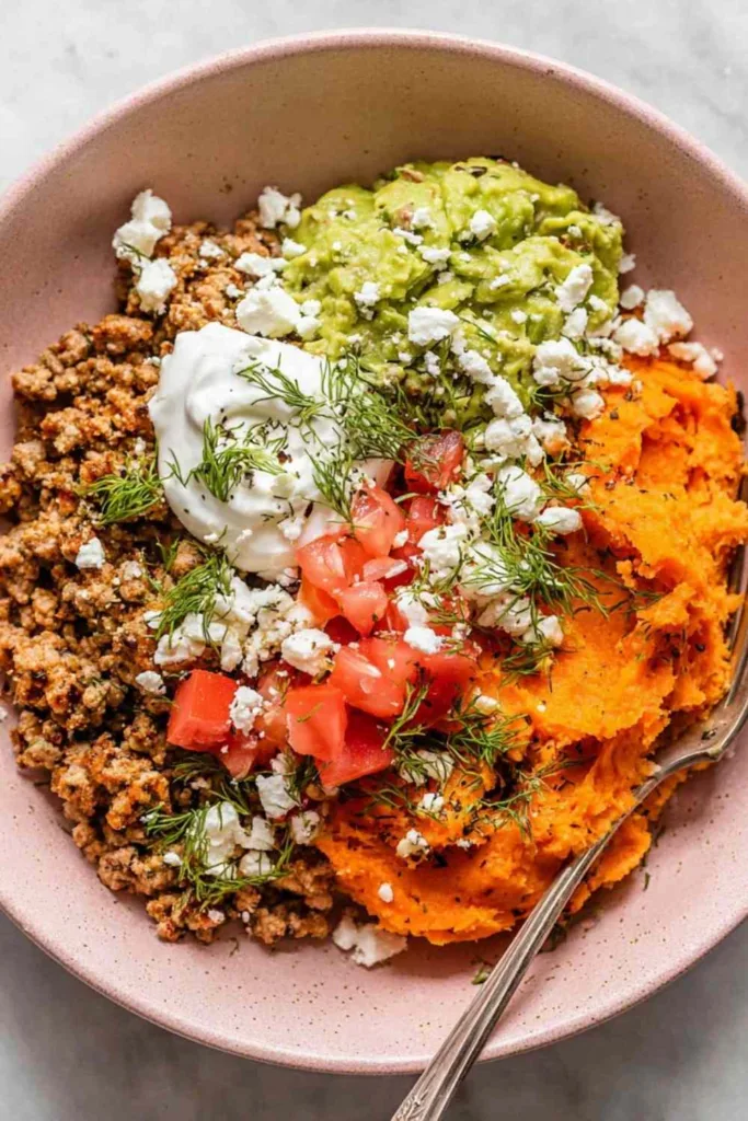 Ground turkey sweet potato bowl topped with guacamole pico de gallo sour cream and queso fresco