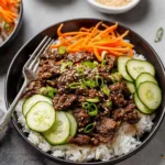 Korean ground beef rice bowl topped with cucumber salad and sliced green onions in a white bowl