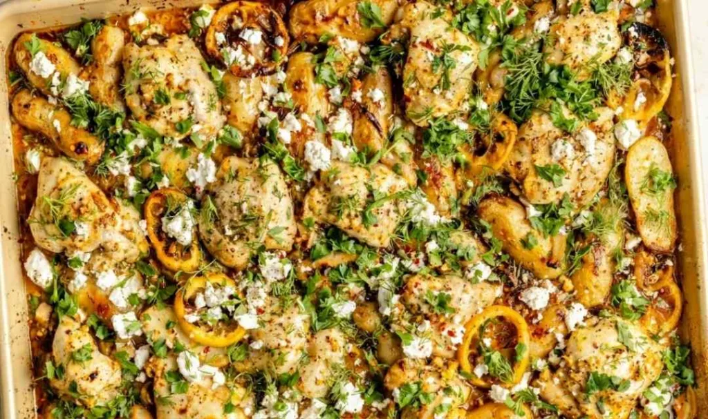 Sheet pan lemon chicken and potatoes topped with crumbled feta, fresh dill, and parsley on a large baking sheet