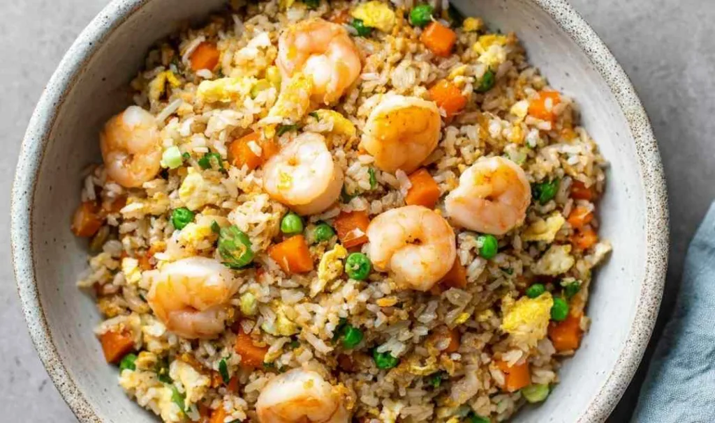 Homemade shrimp fried rice sizzling in a hot wok with green onions, peas, carrots, and scrambled eggs