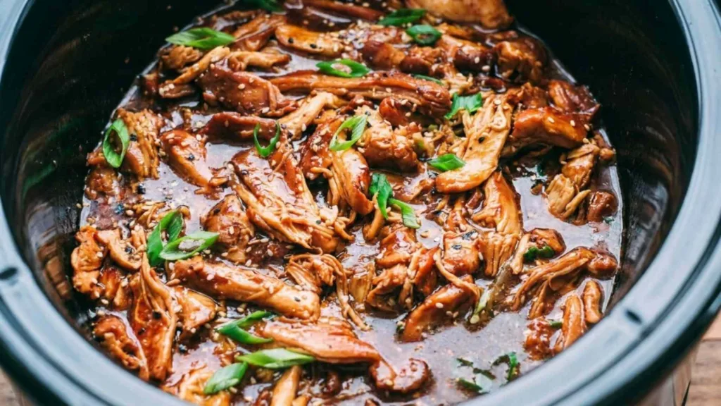 Slow cooker honey garlic chicken shredded in a crock pot with glossy sticky sauce