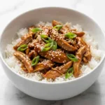 Slow cooker honey garlic chicken shredded in a crock pot with glossy sticky sauce
