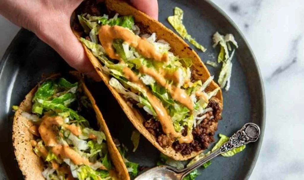 smash burger tacos on a plate topped with melted cheddar shredded lettuce and burger sauce