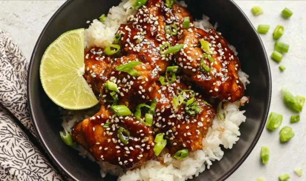 Sticky Asian glazed chicken served over steamed jasmine rice with sesame seeds and green onions on a white plate