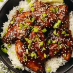 Sticky Asian glazed chicken served over steamed jasmine rice with sesame seeds and green onions on a white plate