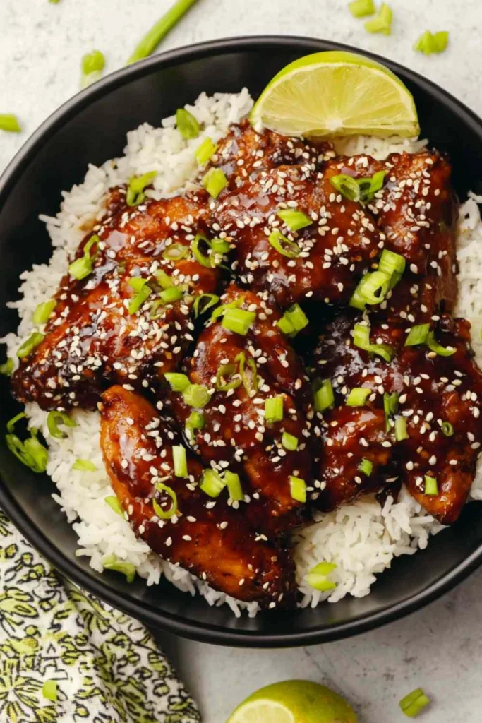Sticky Asian glazed chicken served over steamed jasmine rice with sesame seeds and green onions on a white plate