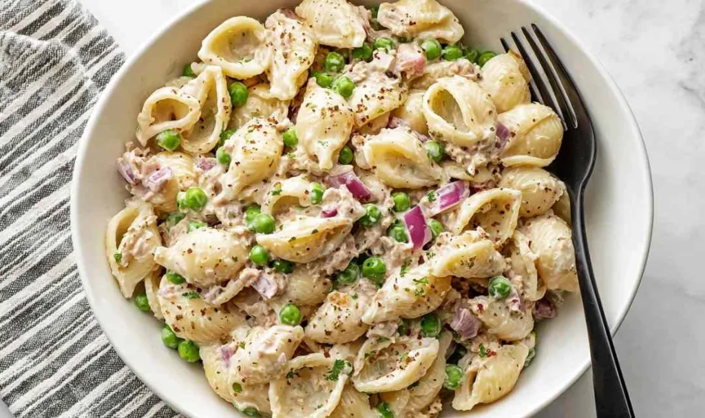 Overhead view of creamy tuna pasta salad with peas and red onion in a white bowl