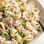 Overhead view of creamy tuna pasta salad with peas and red onion in a white bowl