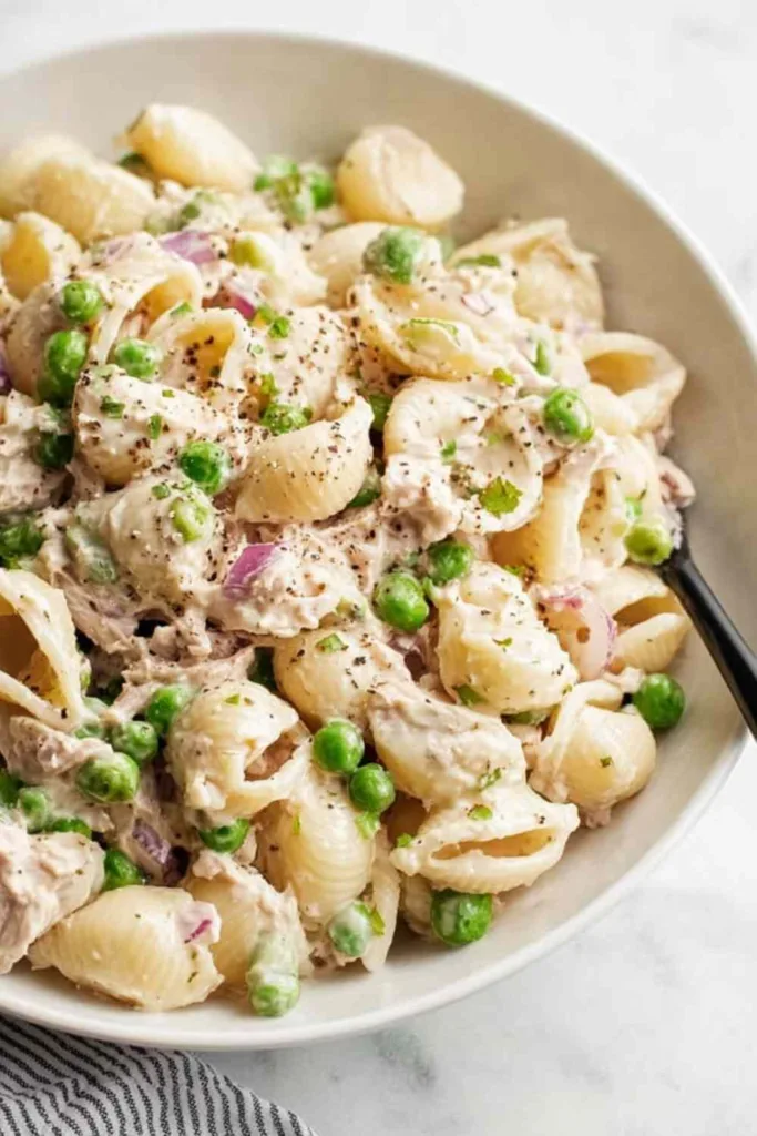 Overhead view of creamy tuna pasta salad with peas and red onion in a white bowl