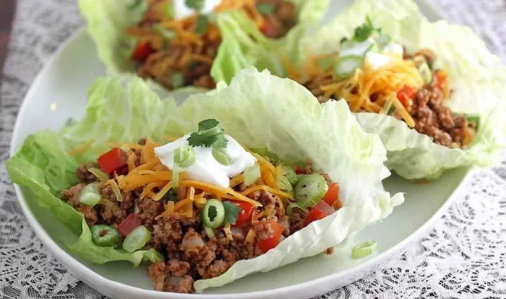 Ground turkey taco lettuce wraps served on a white plate topped with pico de gallo and shredded cheddar