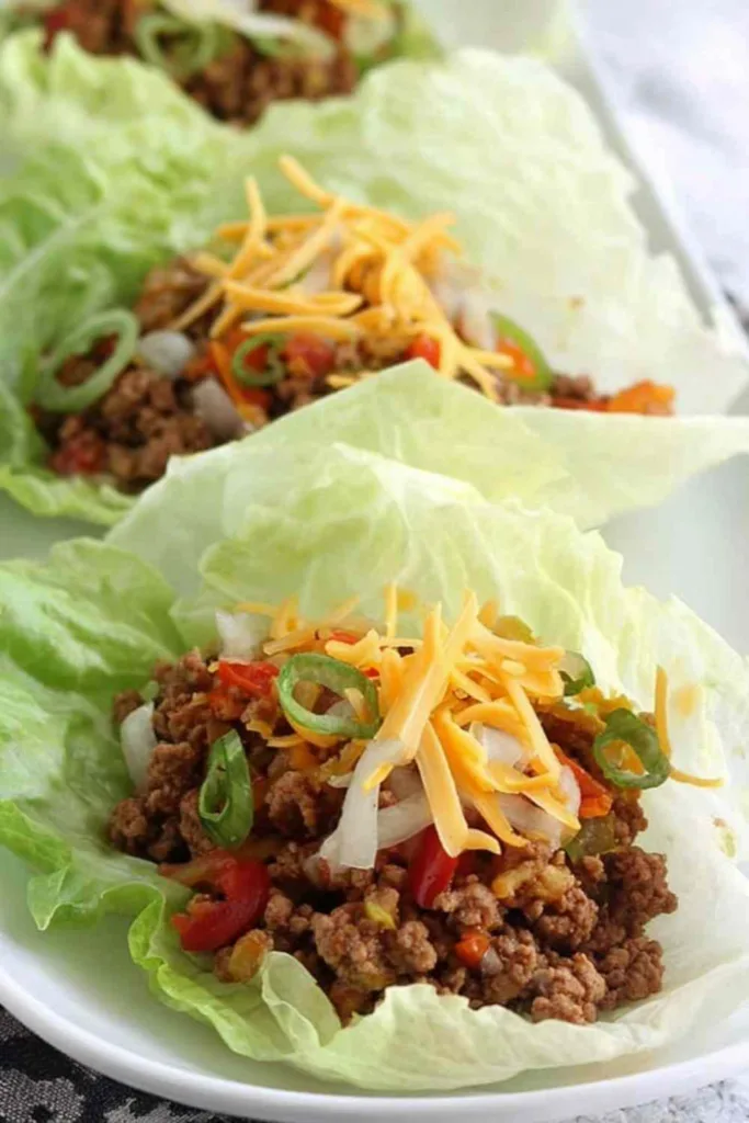 Ground turkey taco lettuce wraps served on a white plate topped with pico de gallo and shredded cheddar
