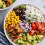 Chicken burrito bowl with cilantro lime rice, chipotle chicken strips, black beans, corn, avocado, and diced tomatoes served in a white bowl