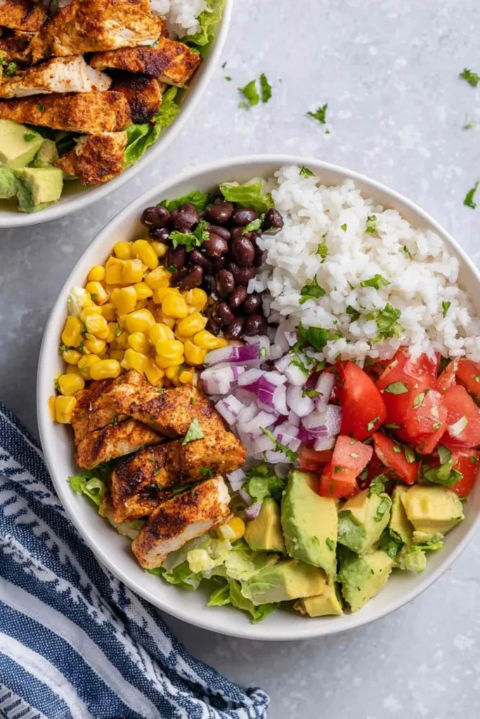 Chicken burrito bowl with cilantro lime rice, chipotle chicken strips, black beans, corn, avocado, and diced tomatoes served in a white bowl