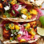 Fish tacos with mango salsa on a white platter with lime wedges and fresh cilantro
