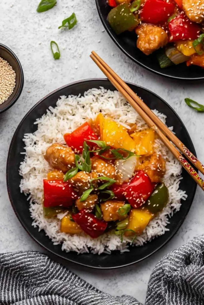 Slow cooker sweet and sour chicken served over white rice with bell peppers and pineapple garnished with green onions and sesame seeds